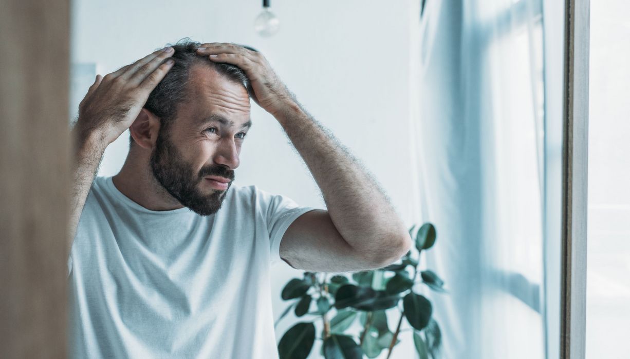 Mann betrachtet seine Haare im Spiegel.