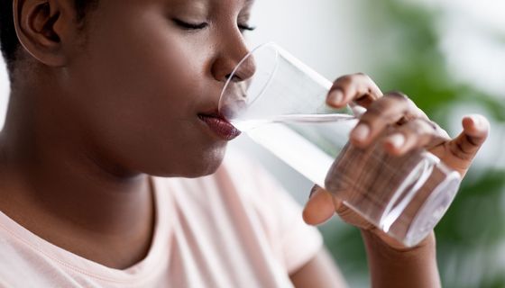 Junge Frau mit Übergewicht, trinkt ein Glas Wasser.