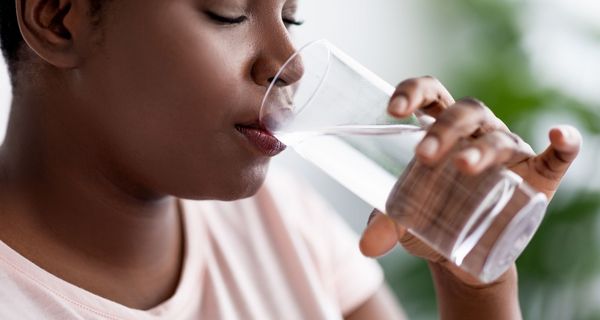 Junge Frau mit Übergewicht, trinkt ein Glas Wasser.