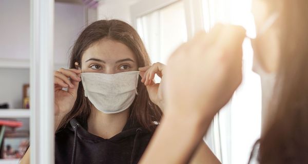 Junges Mädchen, steht vor einem Spiegel und setzt sich eine Maske auf.