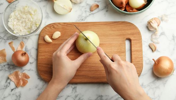 Frau schneidet frische Zwiebel auf Holzbrett am weißen Marmortisch