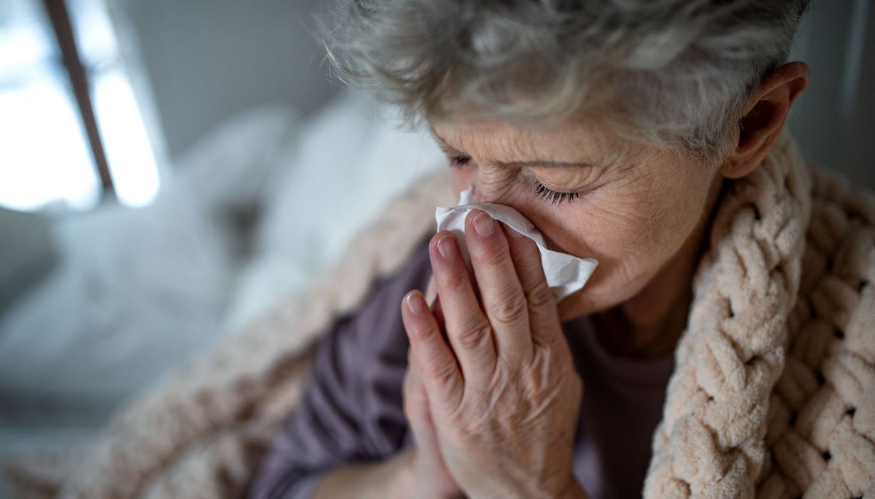 Ältere Frau, zu Hause mit Decke, putzt sich die Nase.
