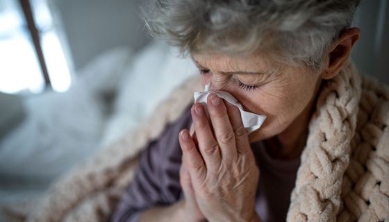 Ältere Frau, zu Hause mit Decke, putzt sich die Nase.
