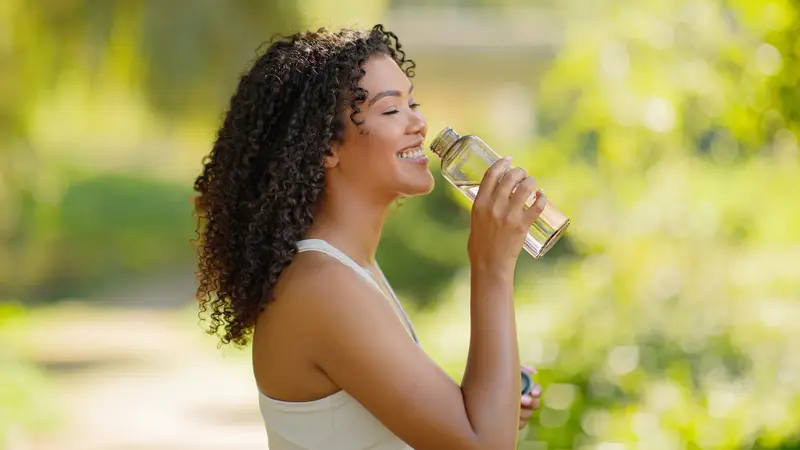 Junge Frau trinkt Wasser aus einer Flasche.