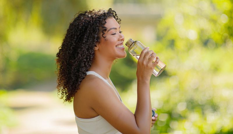 Junge Frau trinkt Wasser aus einer Flasche.