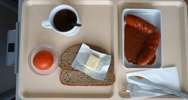 Tablett mit Klinikessen: Wurst, Brot, Butter und eine Tomate.