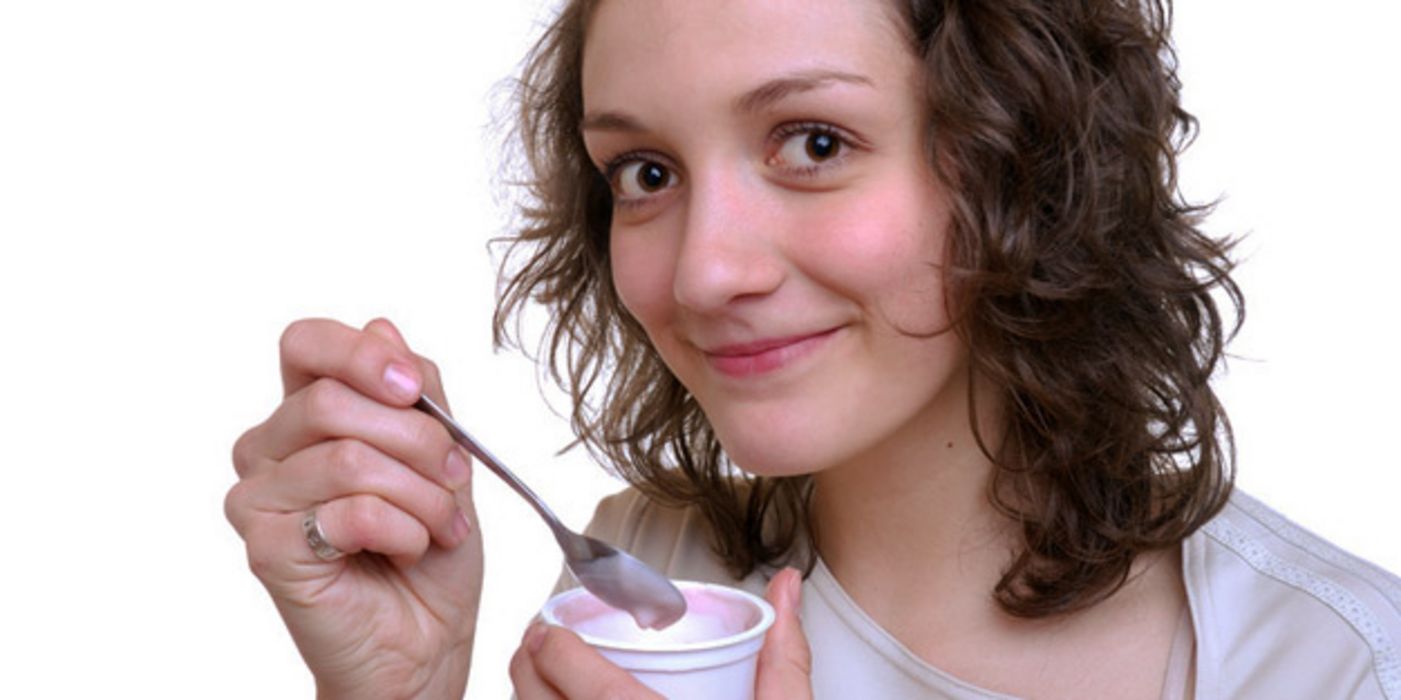 Junge brünette Frau hält einen Becher Joghurt, aus dem sie löffelt