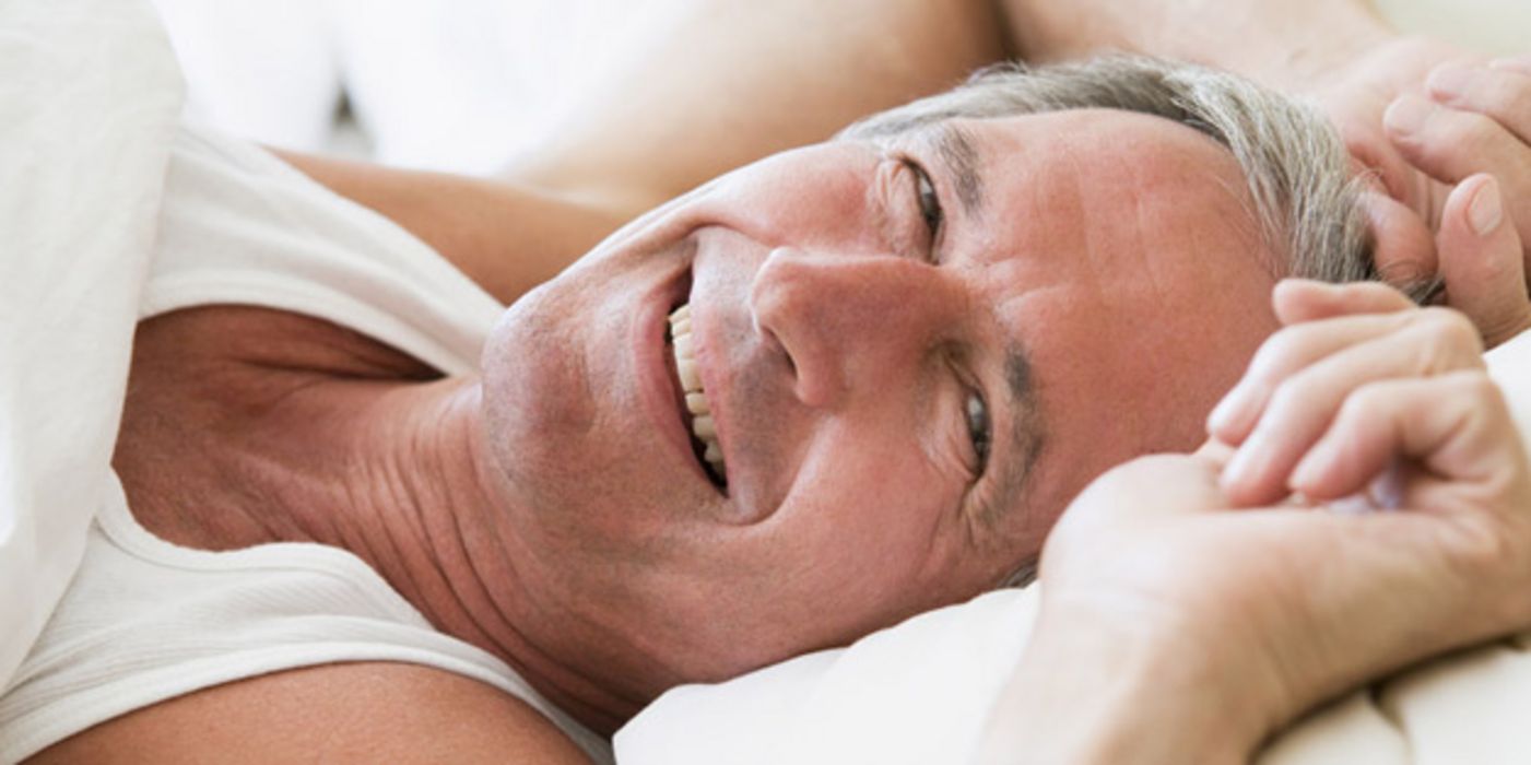 Ausgeschlafener Mann um die 60 beim Aufwachen; lächelt in die Kamera