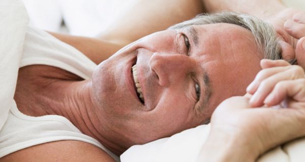 Ausgeschlafener Mann um die 60 beim Aufwachen; lächelt in die Kamera