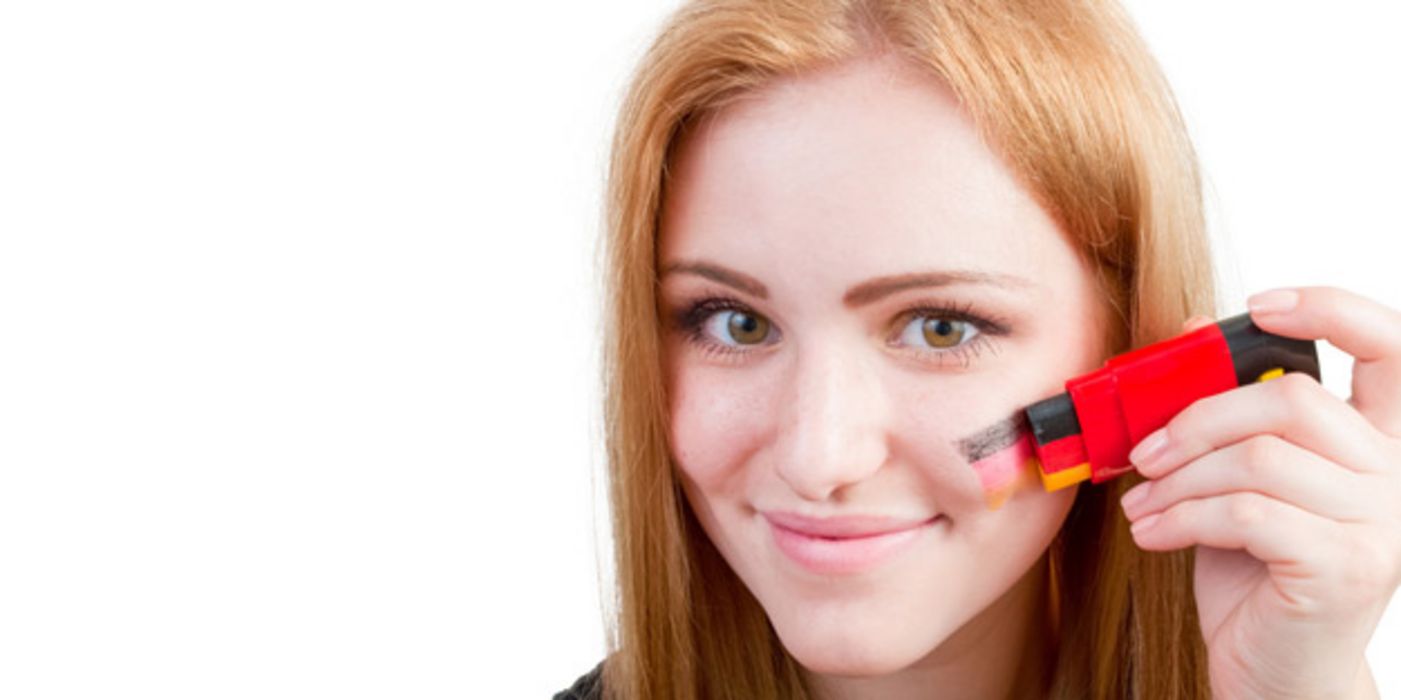 Jugendliche schminkt sich mit Schminkstift eine Deutschlandflagge auf die Wange
