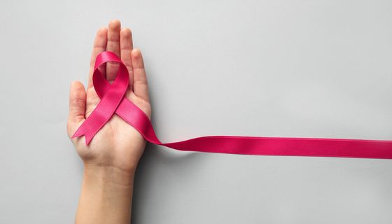 Weibliche Hand, hält eine rosa Schleife als Symbol für Brustkrebs.