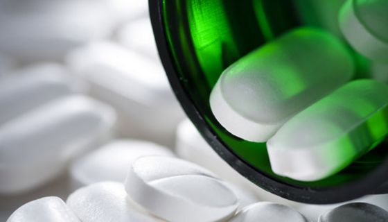 Längliche, weiße Filmtabletten mit Bruchkerbe fallen aus grünem Arzneifläschchen