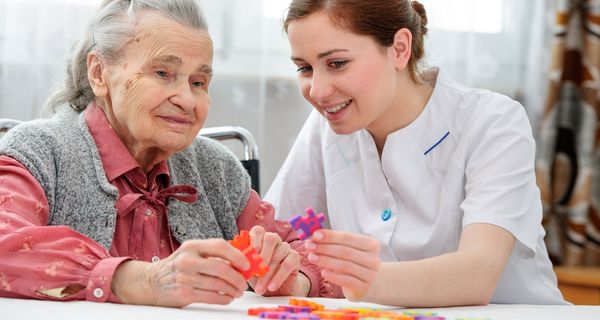 Junge Pflegerin, beschäftigt sich mit Demenz-Patienten und großen Puzzel-Teilen.