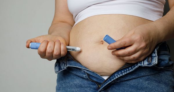 Eine übergewichtige Frau spritzt sich mit der Rechnet Hand ein Medikament in den Bauch.