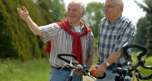 Zwei ältere Männer in Freizeitkleidung stehen in der Natur mit ihren Fahrrädern