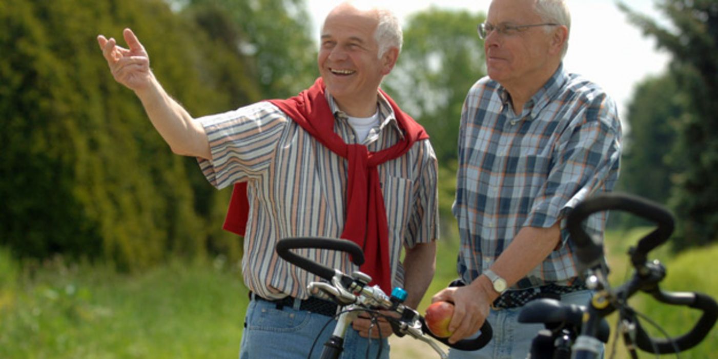 Zwei ältere Männer in Freizeitkleidung stehen in der Natur mit ihren Fahrrädern