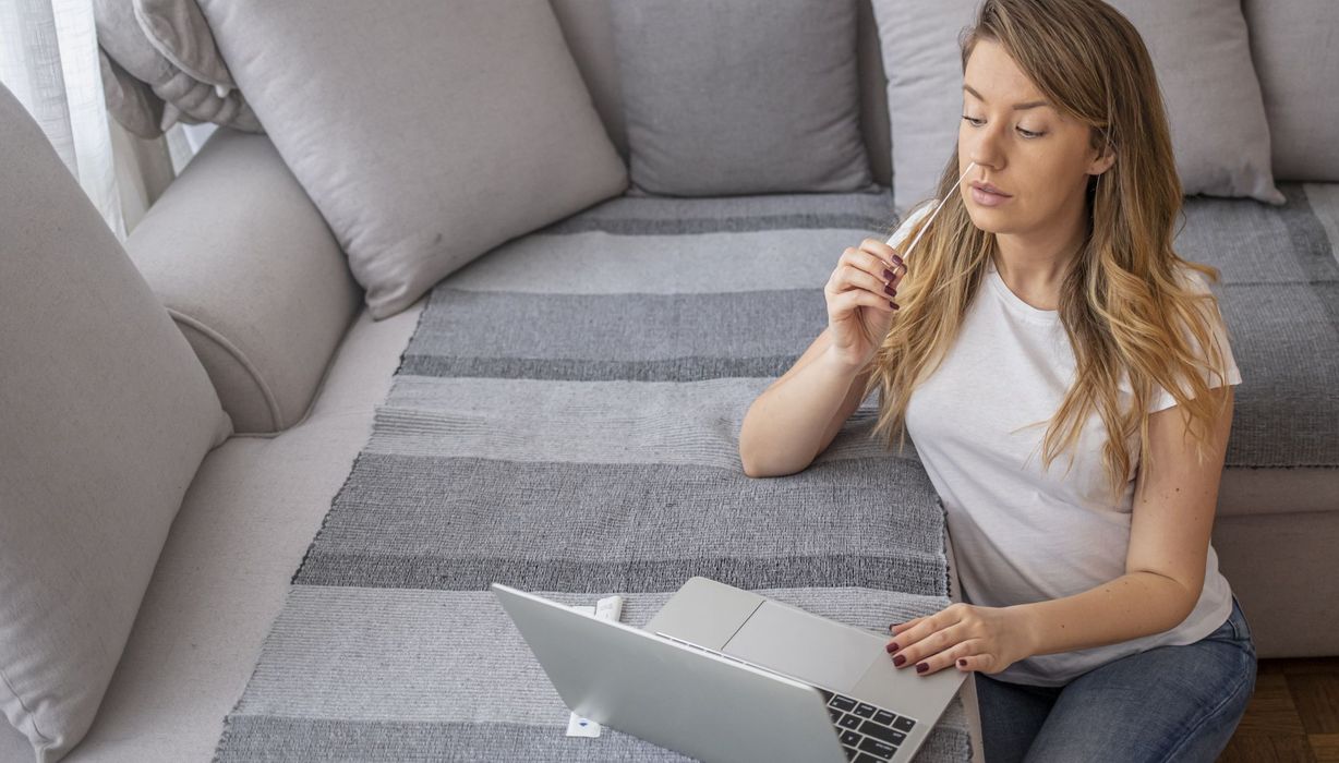 Junge Frau sitzt vor einem Laptop und ist im Begriff, einen Selbsttest zu machen.