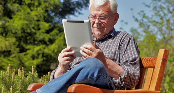 Senior sitzt im Garten und liest in einem Digitalbuch
