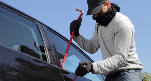 Maskierter Mann bricht Auto auf.