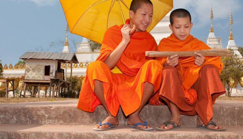 Zwei Asiaten mit orangefarbener Kleidung unter einem Sonnenschirm.