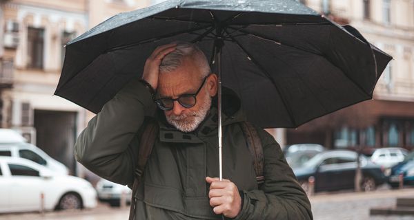 Mann mit Migräne, draußen mit Regenschirm.