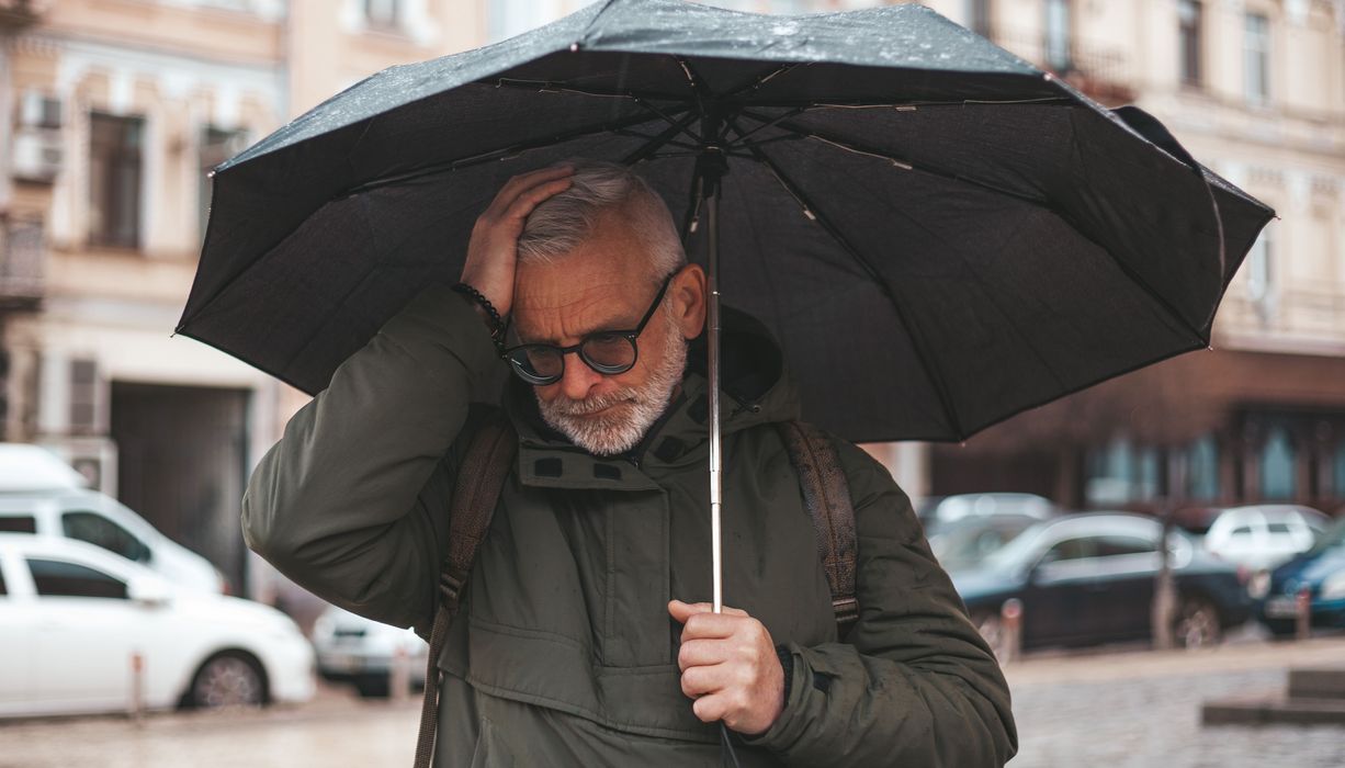 Mann mit Migräne, draußen mit Regenschirm.
