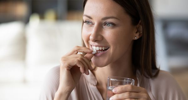 Junge Frau mit Glas Wasser, ist im Begriff, eine Tablette zu schlucken.