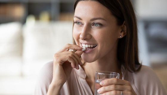 Junge Frau mit Glas Wasser, ist im Begriff, eine Tablette zu schlucken.