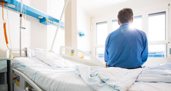 Ein Mann sitzt mit dem Rücken zum Betrachter auf einem Krankenhausbett.