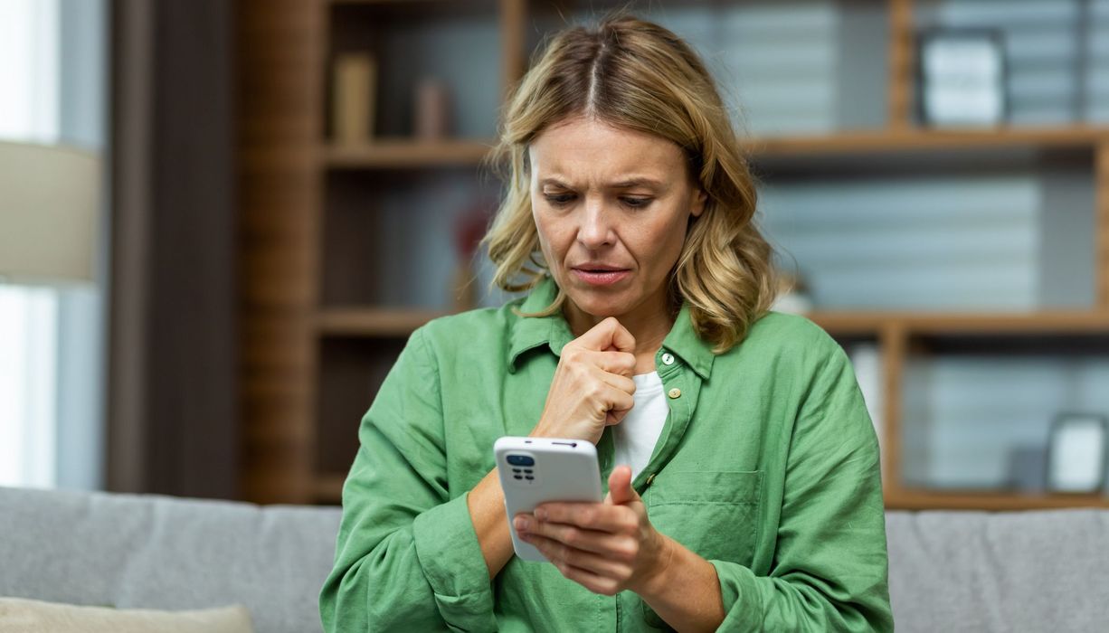 Ältere Frau, schaut nachdenklich auf ihr Smartphone.