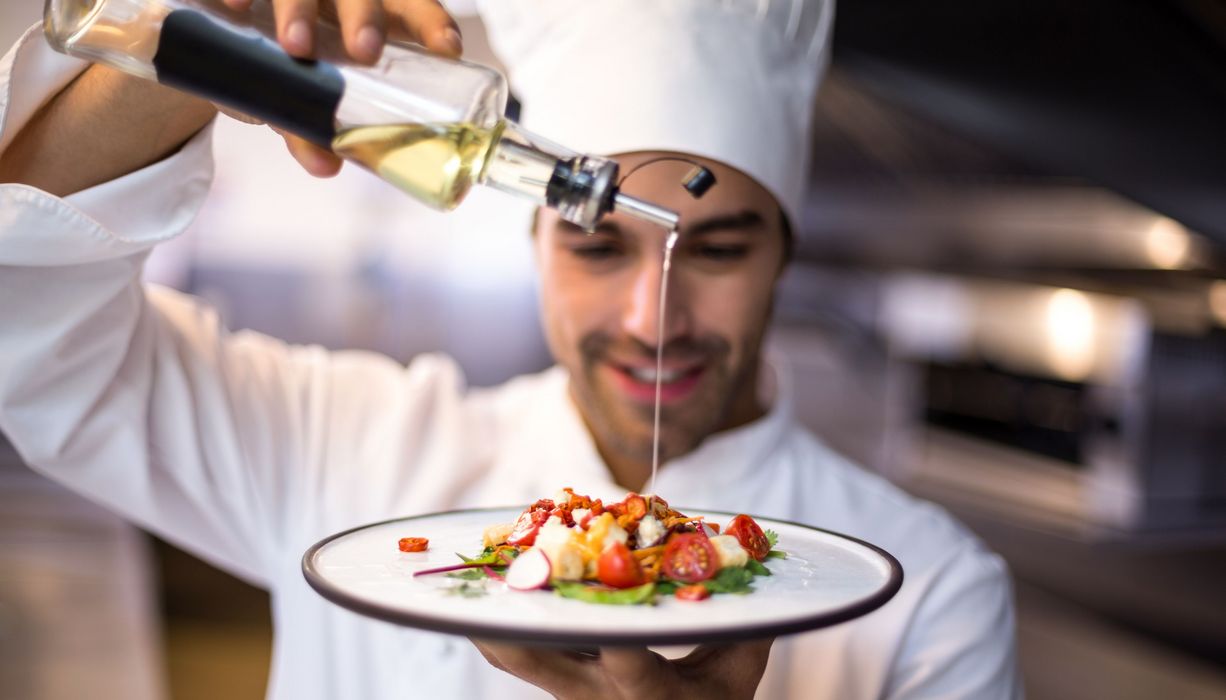 Koch träufelt Öl über einen Salat.