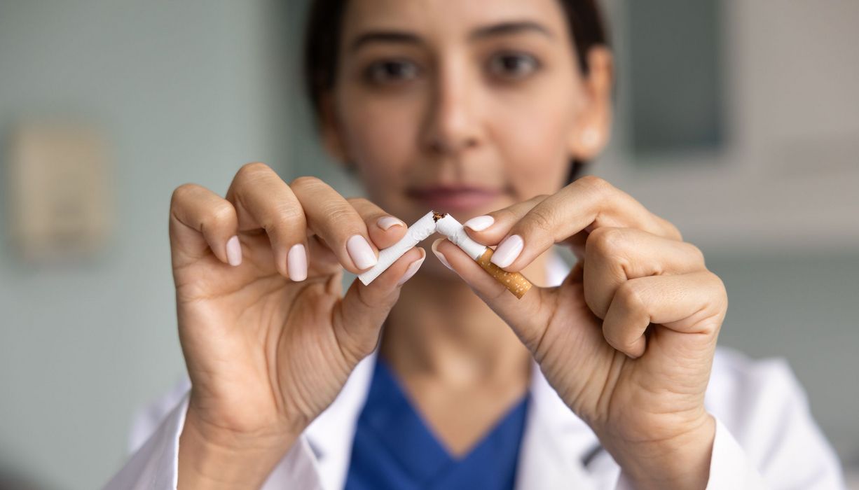 Junge Ärztin (unscharf) zerbricht eine Zigarette (scharf).