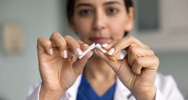 Junge Ärztin (unscharf) zerbricht eine Zigarette (scharf).