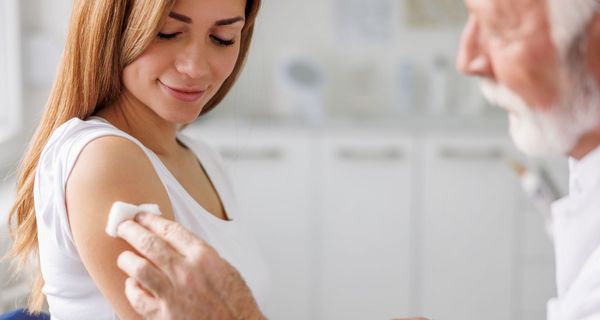 Älterer Arzt desinfiziert den Oberarm einer Frau für eine Impfung.