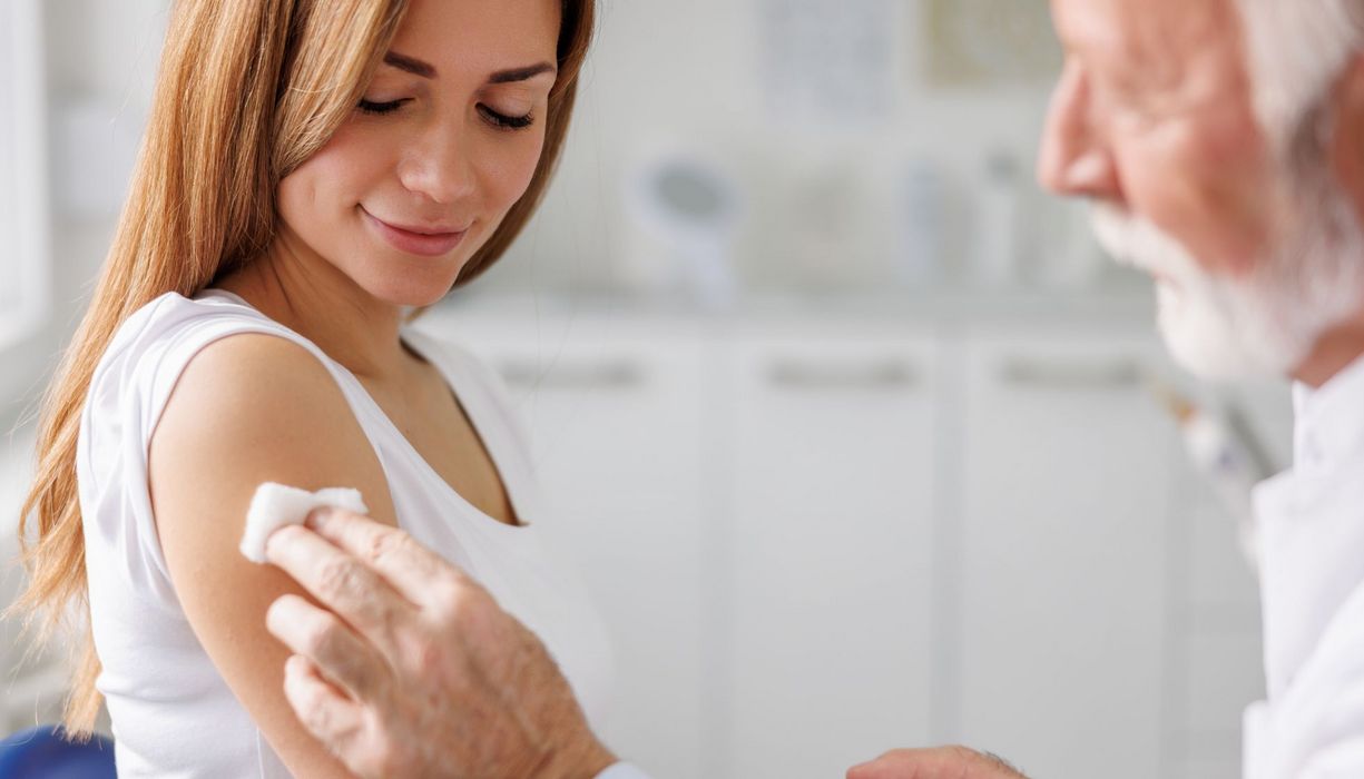 Älterer Arzt desinfiziert den Oberarm einer Frau für eine Impfung.