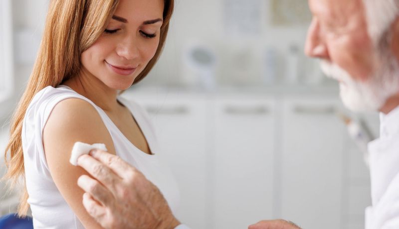 Älterer Arzt desinfiziert den Oberarm einer Frau für eine Impfung.