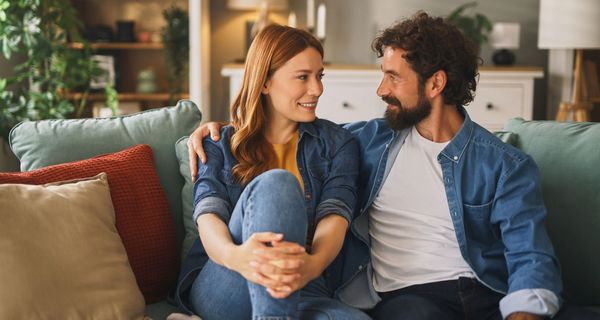 Ein Mann und eine Frau sitzen gemeinsam auf dem Sofa. Er hat seinen Arm um sie gelegt.