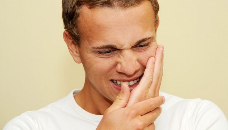 Junger Mann fasst sich vor lauter Zahnschmerzen an die Wange