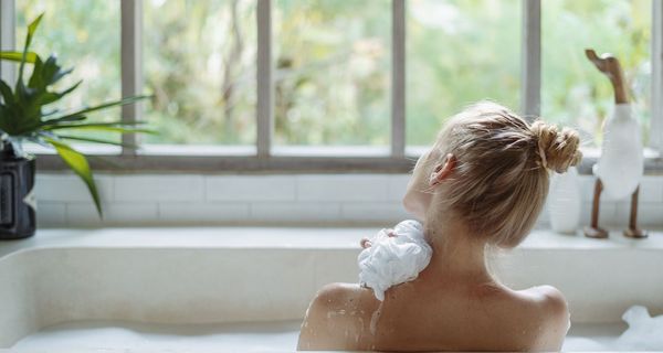 Frau, sitzt in einer Badewanne und schaut nach draußen.