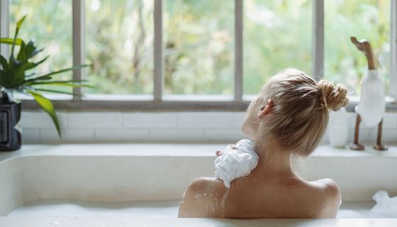 Frau, sitzt in einer Badewanne und schaut nach draußen.