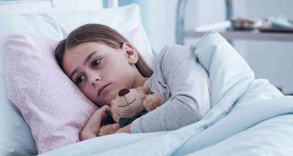 Ein trauriges Mädchen liegt im Krankenhaus, einen Teddybär im Arm.