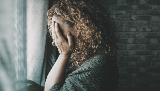 Frau steht vor dem Fenster und bedeckt ihr Gesicht mit ihren Händen.