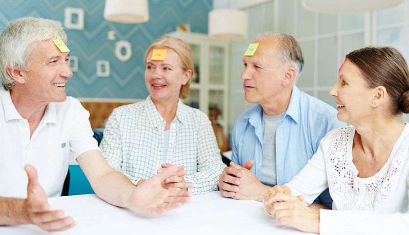 Vier Personen über 65 sitzen an einem Tisch und spielen "Wer bin ich?".