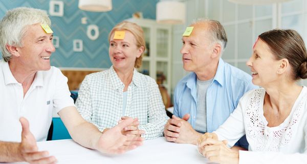 Vier Personen über 65 sitzen an einem Tisch und spielen "Wer bin ich?".