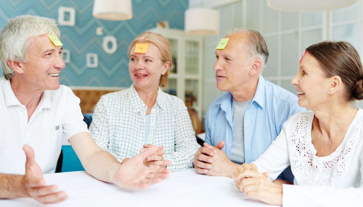 Vier Personen über 65 sitzen an einem Tisch und spielen "Wer bin ich?".