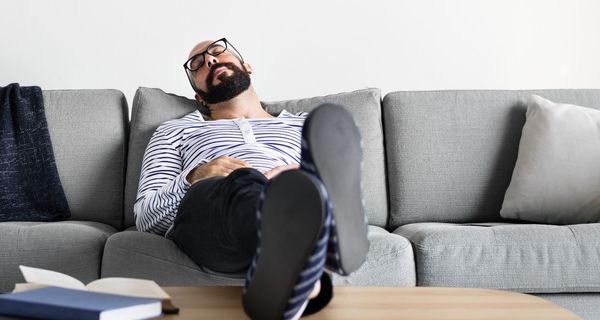 Ein mittelalter Amnn sitzt auf dem Sofa und hält ein Nickerchen.