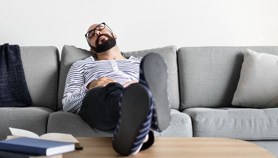 Ein mittelalter Amnn sitzt auf dem Sofa und hält ein Nickerchen.