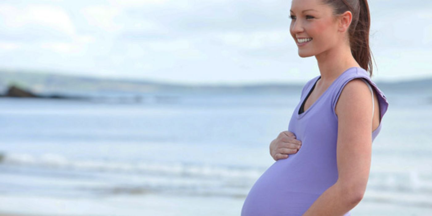 Junge, schwangere Frau am Strand