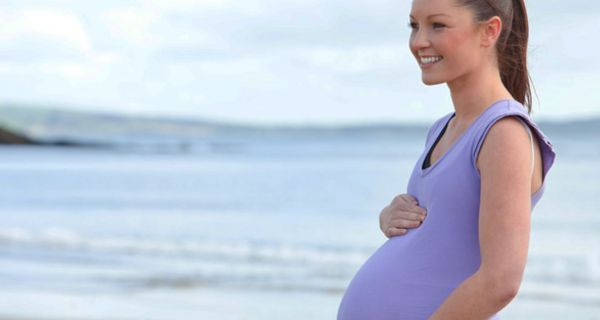 Junge, schwangere Frau am Strand