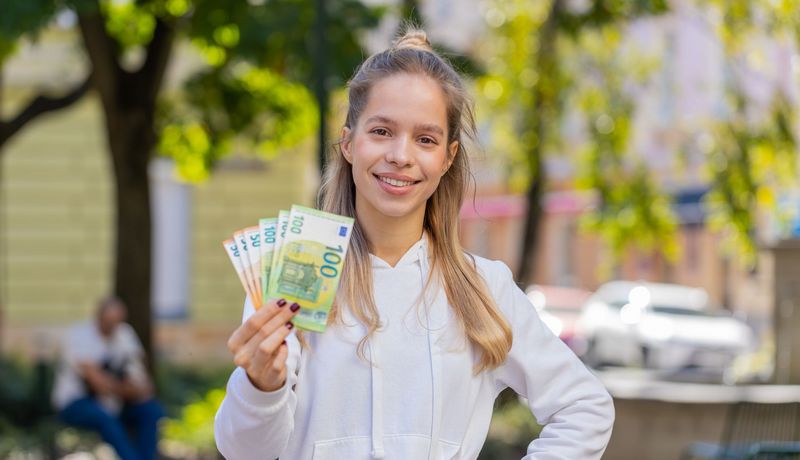 junge Frau hält fröhlich 50- und 100-Euro-Scheine